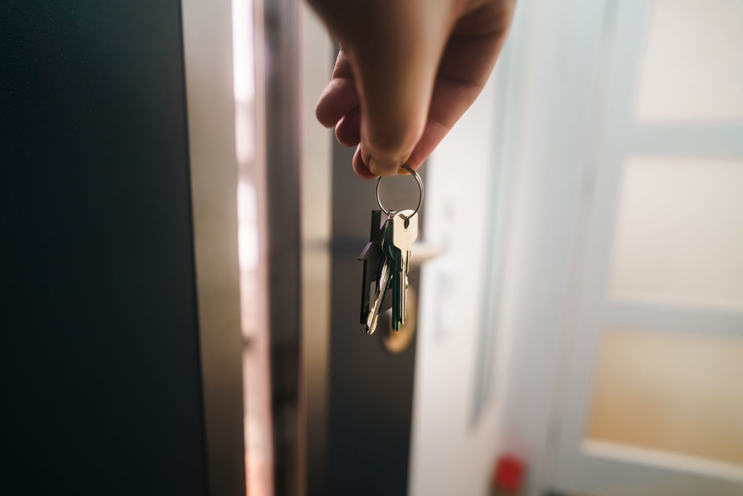 Hand holding a ring of house keys beside an open front door