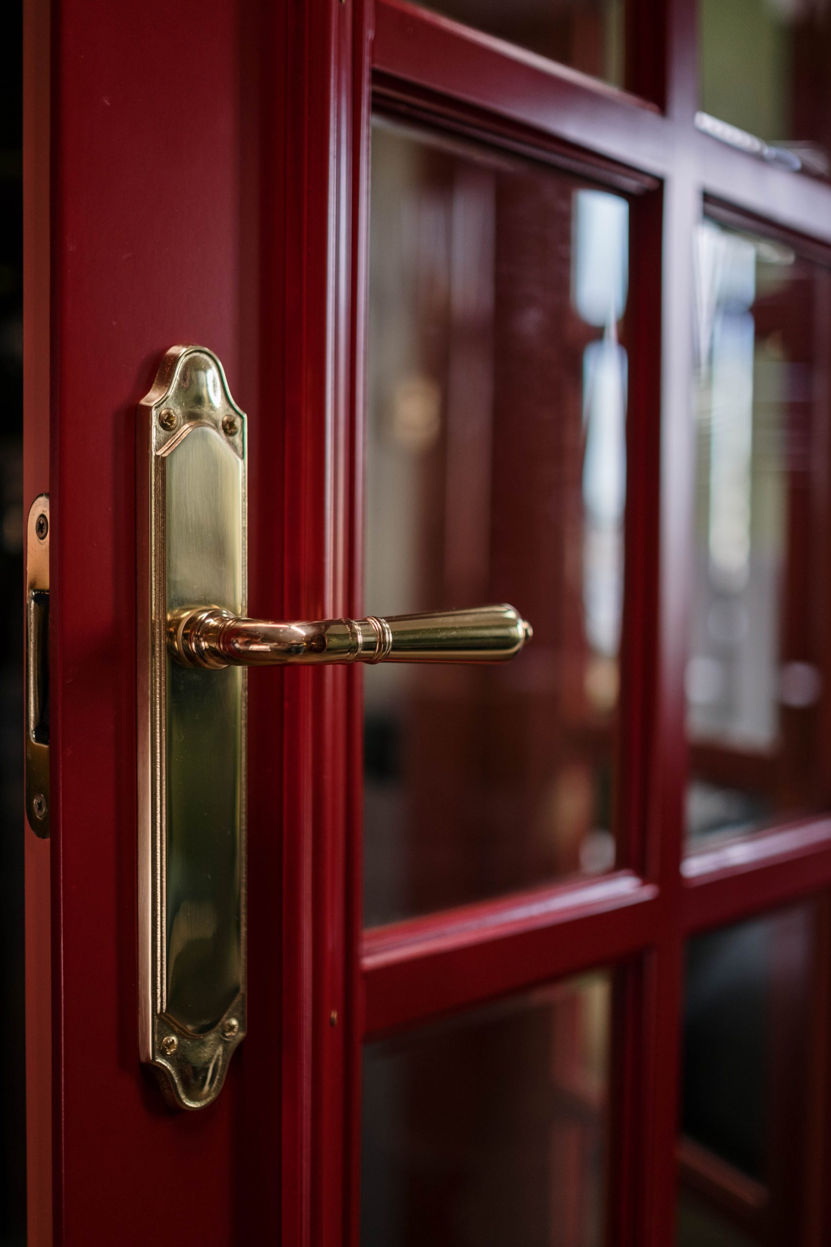 Brass lever handle and latch on a partially open red glass-paneled door